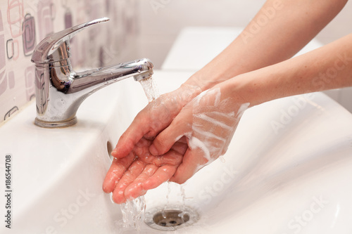 A woman is washing soap foam from her hands under running water. Hygiene. Washing hands in the bathroom