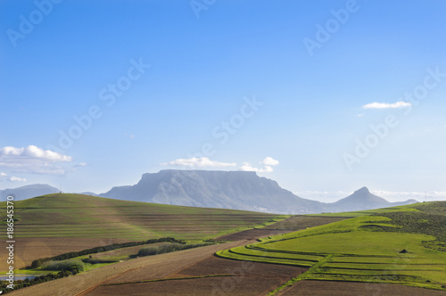 View of Table mountain in Cape Town, South Africa over vistas of wine lands and vineyards on a sunny day with clear blue skies and scattered clouds.