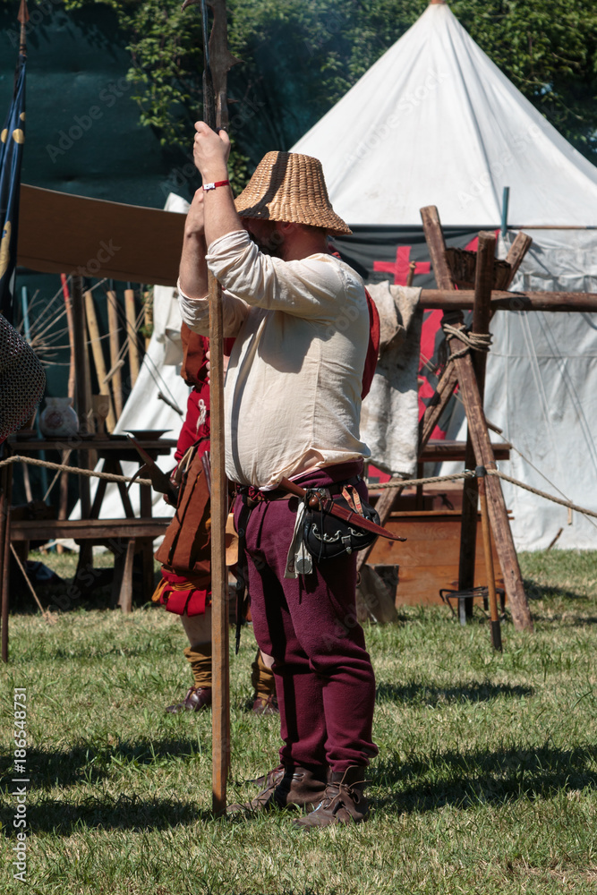 Guard with Pole Weapon and Straw Hat during Medieval Event Fair near White Tent