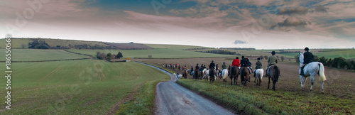 Panorama of Boxing Day hunt crossing South Downs landscape towards Old Winchester Hill iron age fort on a cold winters day with bright sunshine