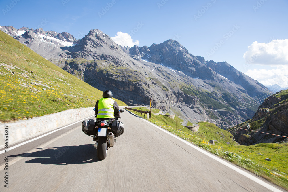 Motorradfahrer fährt mit seinem Motorrad auf kurvigen Straßen durch die Berge und einer wunderschöne Landschaft