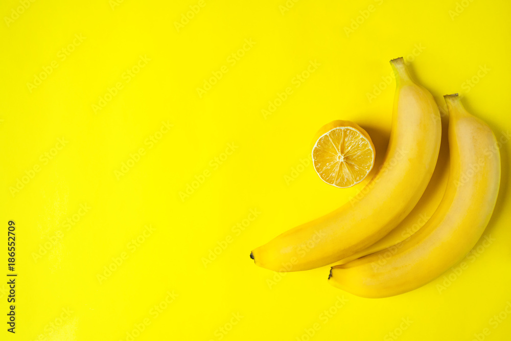 Yellow bananas and sliced lemon on a yellow background with place for text. Bright colors. Flat lay