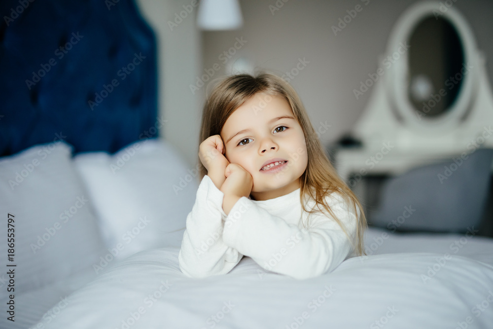 Portrait of little girl hugging pillow while sitting on bed and looking at camera in the morning Portrait of little girl hugging pillow while sitting on bed and looking at camera in the morning
