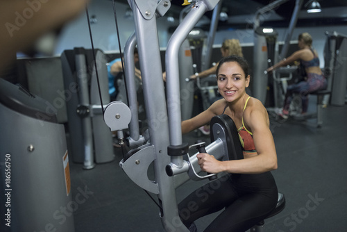 Young woman training at gym in exercise machine, pectoral contractor training.