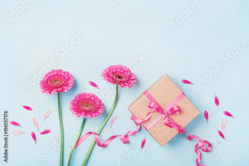 Spring composition with pink flowers and gift box on blue table top view. Greeting card for Birthday, Woman or Mothers Day. Flat lay.