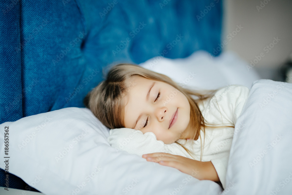Close-up portrait of beautiful little kid lying on bed with hand under pillow, looking at camera at home Close-up portrait of beautiful little kid lying on bed with hand under pillow, looking at camera at home