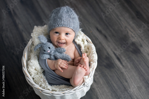 Sweet baby boy in basket, holding and hugging teddy bear, looking curiously at camera