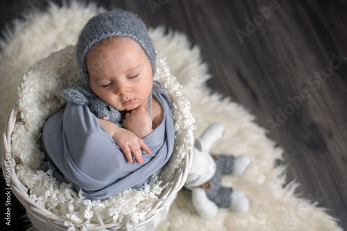 Sweet baby boy in basket, holding and hugging teddy bear, peacefully sleeping