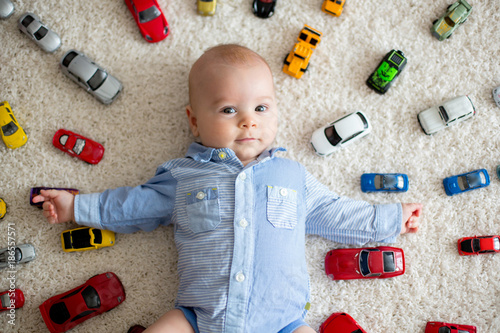 Adorable baby boy, lying on the floor, toy cars around him