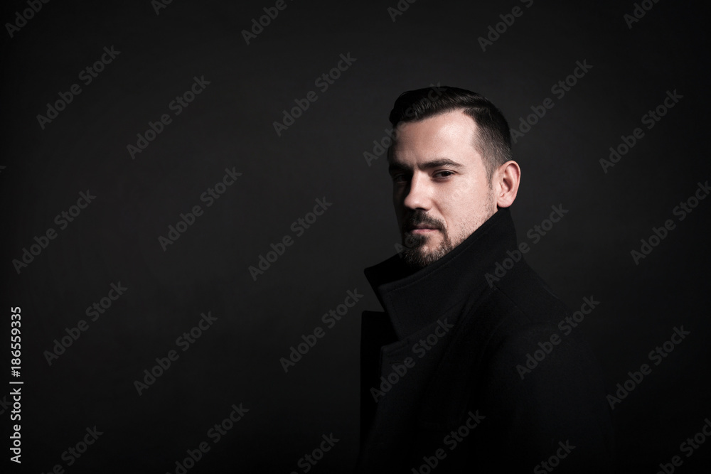 Portrait of a stylish young man in a black coat. Black background. Portrait of a stylish young man in a black coat. Black background.