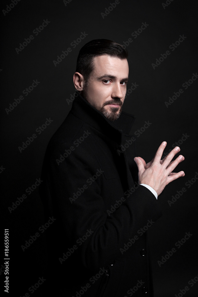 Portrait of a stylish young man in a black coat. Black background.