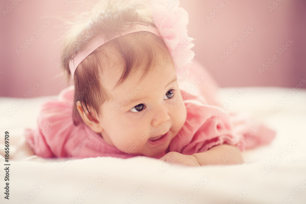 Cute little baby girl lying in the bed in pink dress. Three month old infant child on white soft blanket Cute little baby girl lying in the bed in pink dress. Three month old infant child on white soft blanket