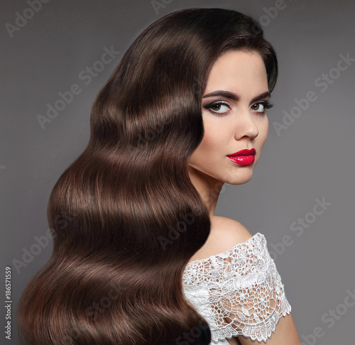 Wavy hair. Beauty brunette red lips makeup and long healthy shine hairstyle. Beautiful face of female model isolated on grey studio background.