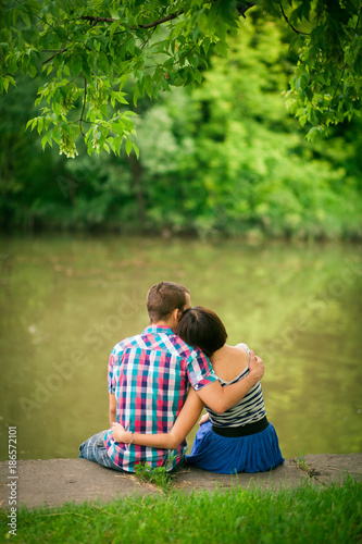 the couple in an embrace sits on the river bank