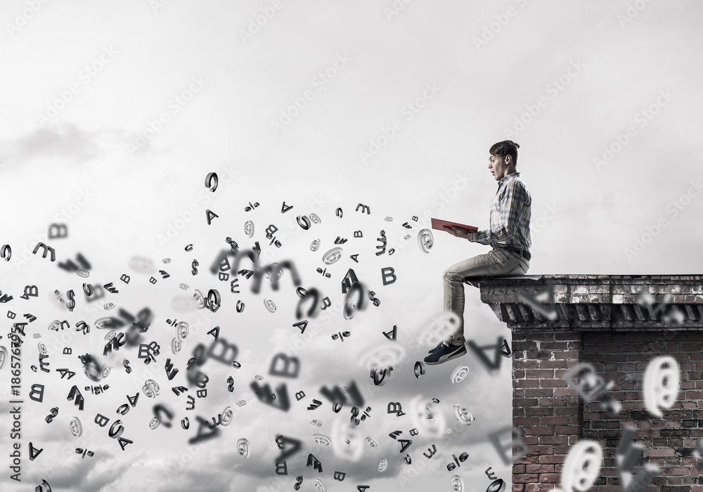 Man on roof edge reading book and symbols flying around Man on roof edge reading book and symbols flying around