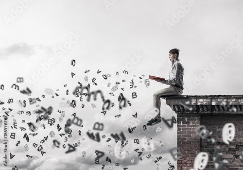 Man on roof edge reading book and symbols flying around