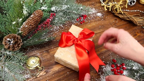 Christmas wooden background with snowy branch Top view. The hands of a young girl put a gift with a red bow on the table