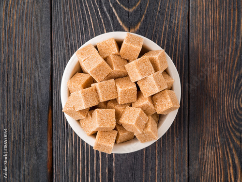 cubes of cane sugar in white bowl on wooden table, close-up, side view