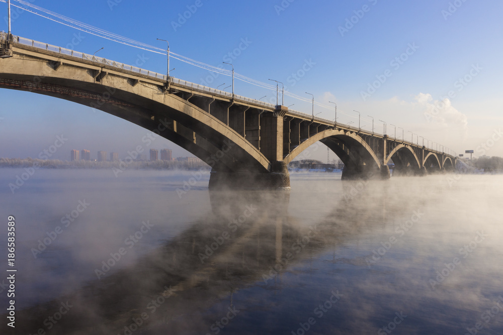Cityscape with a Bridge Communal over the Yenisei river in Krasnoyarsk in winter amazing evening. The bridge is reflected in the mirror-like surface of the water