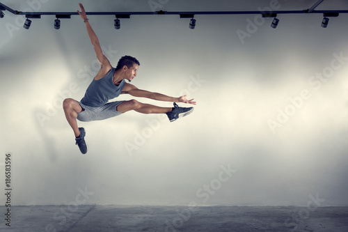 Young man jumping in front of gray wall