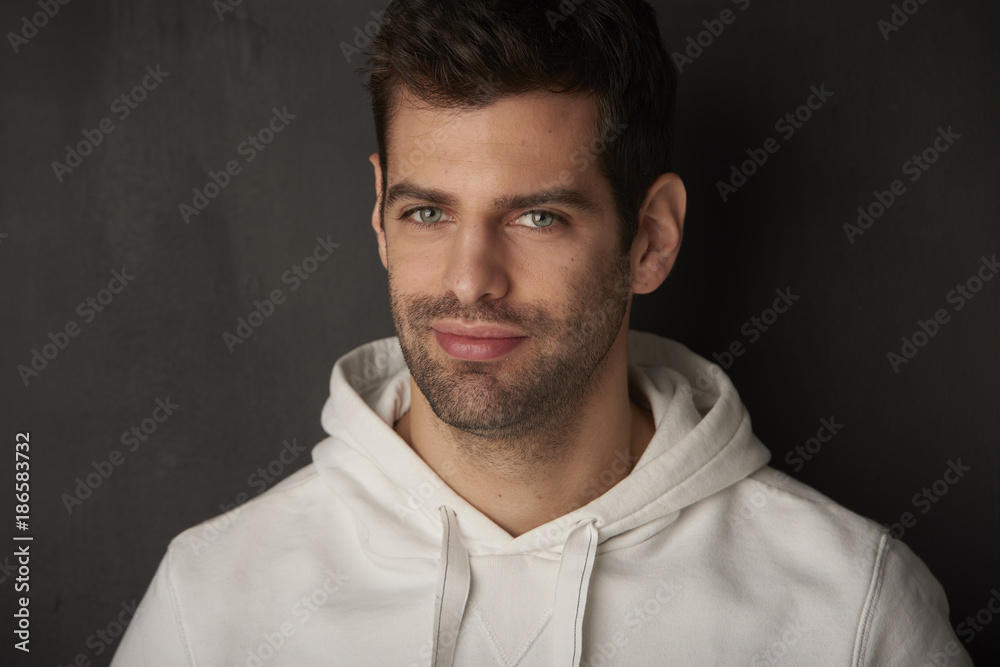 Obraz premium Studio shot of a handsome young man sitting at dark background while looking at camera and smiling.