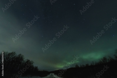 Northen lights in green stars and borealis in an show with a road lit up