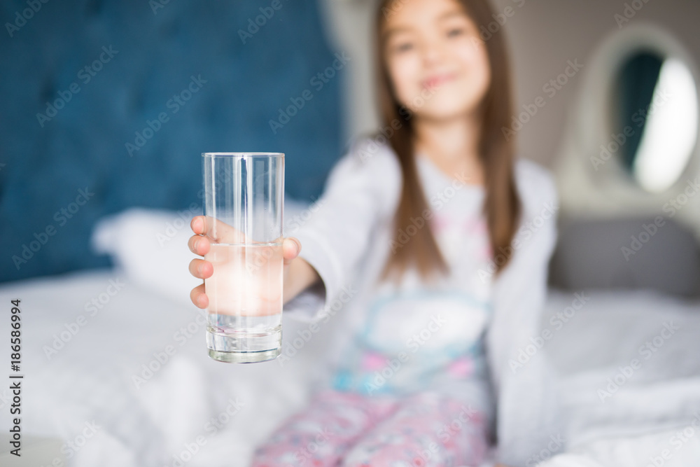 Beautiful little girl drinking water on white bed at home Beautiful little girl drinking water on white bed at home