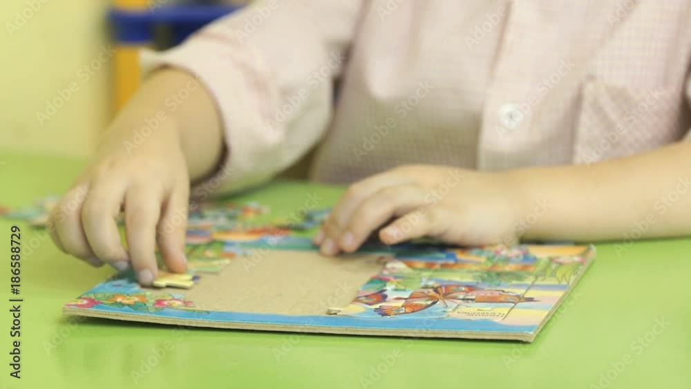 Close-up of hands of little unidentified child collecting picture from puzzles at the table in kindergarten Close-up of hands of little unidentified child collecting picture from puzzles at the table in kindergarten