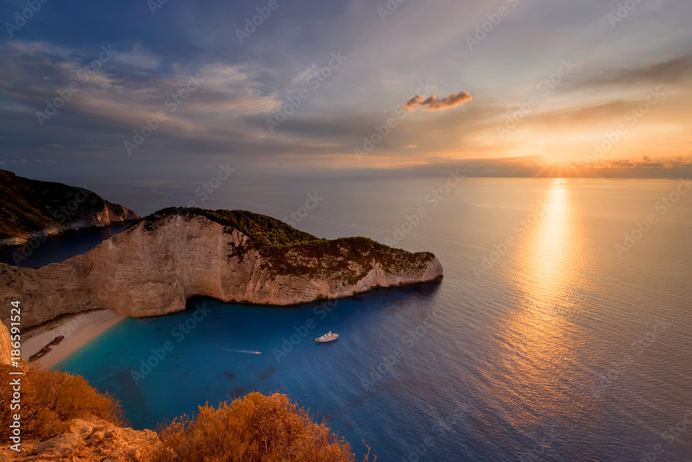Sunset scenery with sun disc falling behind Ionian sea at Navagio beach with shipwreck view, Zakynthos - Zante island in Greece. Very popular and famous travel destination for summer vacations.
