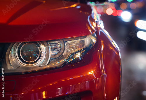 Headlights and hood of sport red car. evening city. Automobile detail close-up