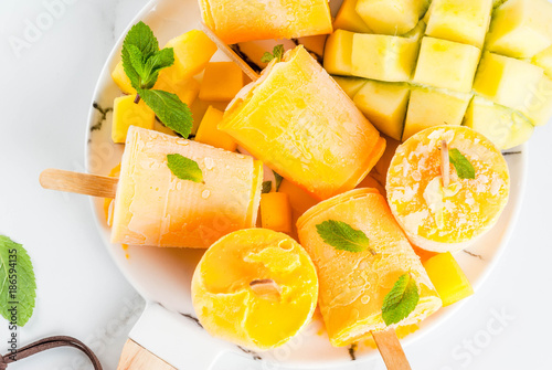 Ice cream, popsicles. Organic dietary foods, desserts. Frozen mango smoothie, with mint leaves and fresh mango fruit, on plate, on white marble table. Copy space