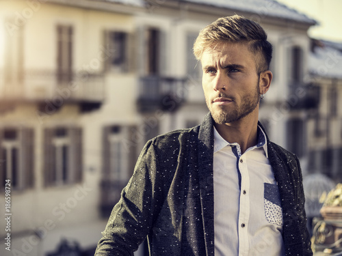 Handsome trendy blond man standing outdoor in European city setting with elegant old historic building behind
