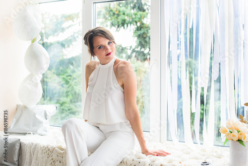 A beautiful and young girl in a white living room at home is happy at the window. A woman symbolizes beauty, youth, love and health Free Download A beautiful and young girl in a white living room at home is happy at the window. A woman symbolizes beauty, youth, love and health - GFXLoad