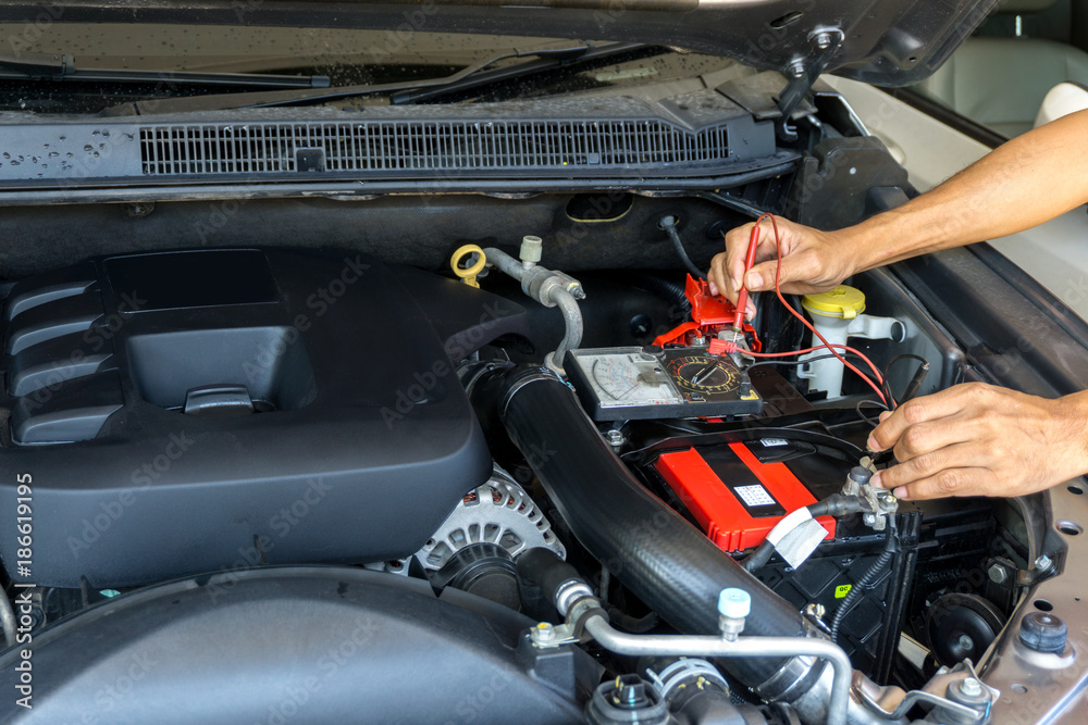 Mechanic car service using  Multimeter  to check the voltage level in a car battery. 