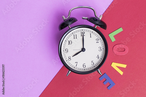 Vintage black alarm clock on two tone color pink and red background and word LOVE , Concept Time of Valentine day