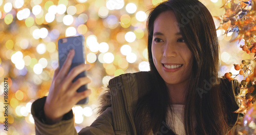 Woman taking photo on cellphone with christmas tree decoration at night