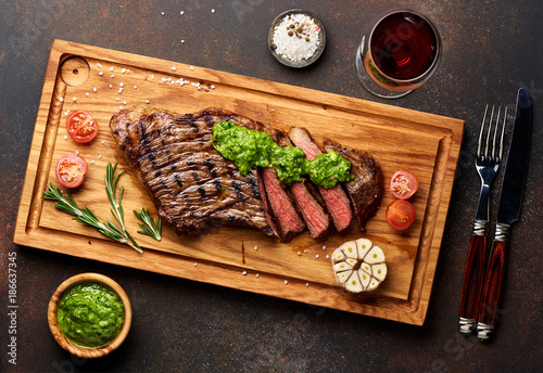 Grilled Black Angus Steak and a glass of red wine with chimichurri sauce on meat cutting board. photo