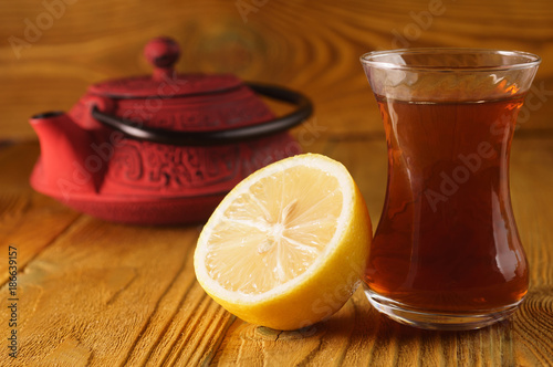 A cup of black tea, a lemon, a teapot on a wooden background