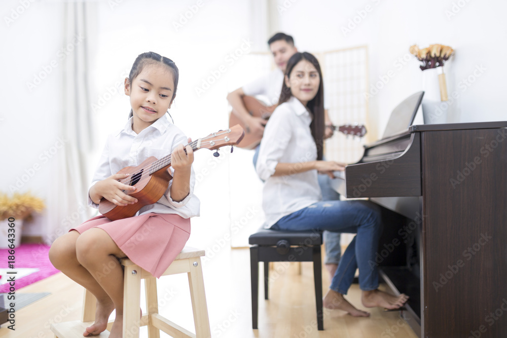Asian family,daughter playing ukulele,father playing guitar,mother playing piano Asian family,daughter playing ukulele,father playing guitar,mother playing piano
