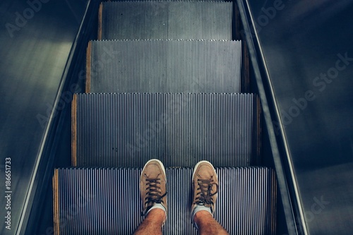 Selfie of feet in sneaker shoes on escalator steps, top view in vintage style photo