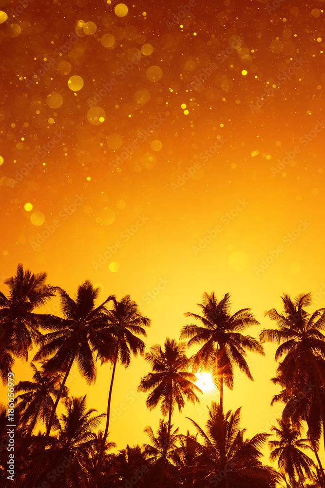 Palm trees silhouettes on tropical beach at summer warm vivid sunset with party glitter bokeh overlay effect