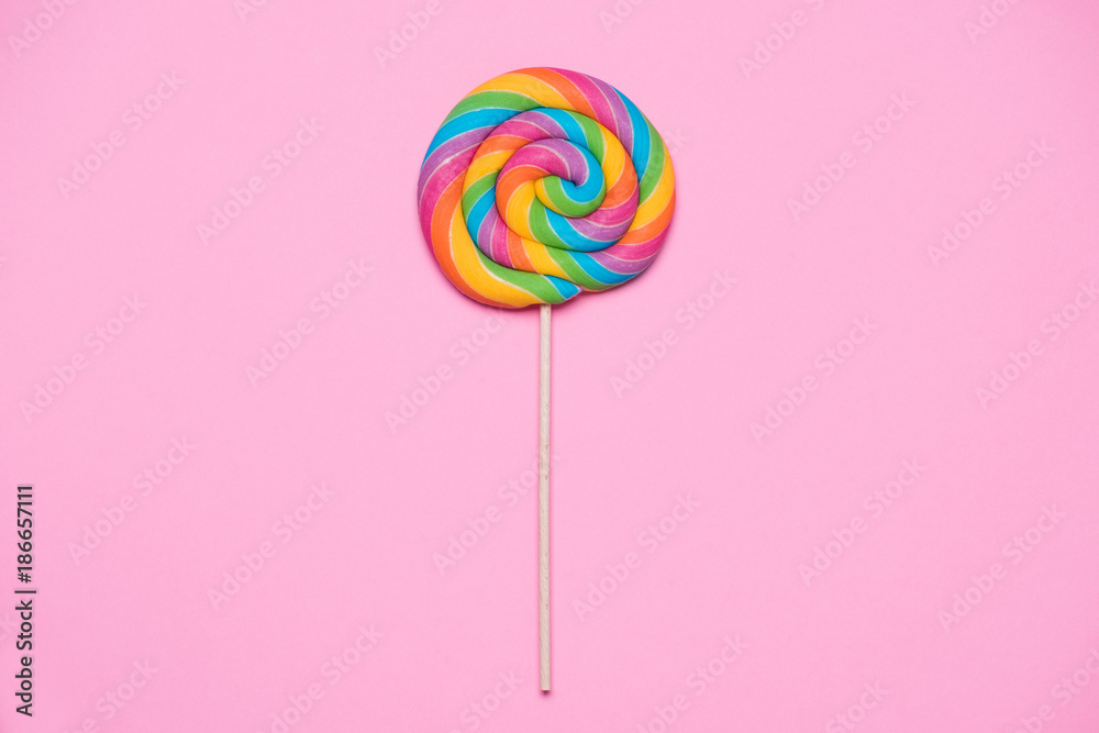 Lollipop swirl on wooden stick on pink paper background Lollipop swirl on wooden stick on pink paper background