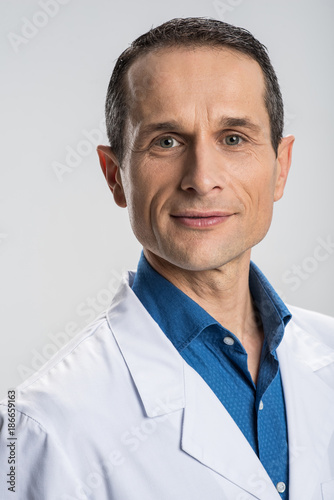 All attention. Thoughtful reflective male physician standing on the isolated background while smiling and looking straight  © Viacheslav Yakobchuk