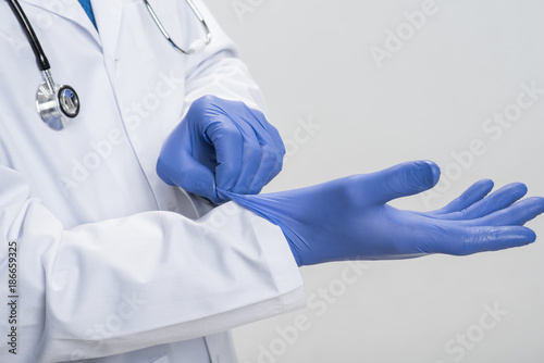 Preparation for surgery. Close up of professional  male hands in process of putting   on latex gloves while standing on the grey background