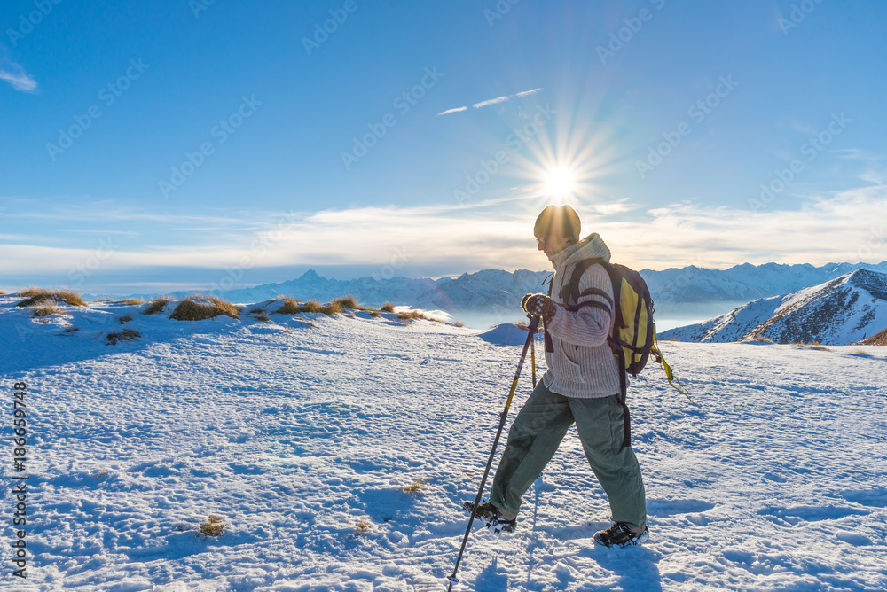 Woman backpacker trekking on snow on the Alps. Rear view, winter lifestyle, cold feeling, sun star in backlight.
