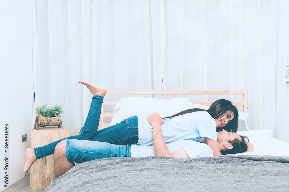 Mixed race lovers concept. Young white male in his bedroom getting intimate with his pretty young chinese girlfriend. Wearing blue jeans, blue shirt and in their early twenties. Taken indoor.
