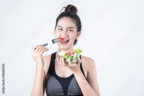 Fitness and health concept. Portrait of fit sport woman holding green salad bowl trying to eat, isolated on white background. Chinese woman with black tank top and pants.