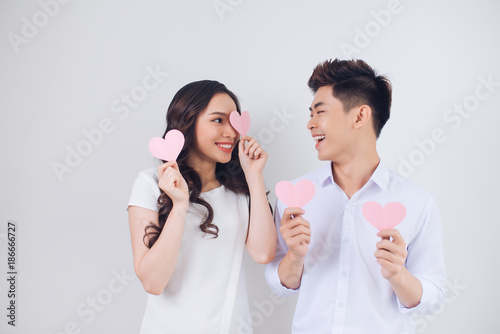 Happy young Vietnamese couple is holding pink paper hearts and smiling