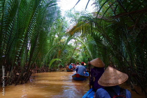 My Tho, Vietnam: Tourist at Mekong River Delta jungle cruise with unidentified craftman and fisherman rowing boats on flooding muddy lotus field in Mekong delta into Ho Chi minh city