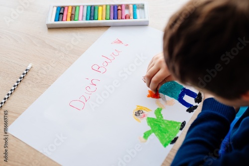 8 letni chłopiec maluje kredkami obrazek lurkę dla swojej babci na Dzień Babci